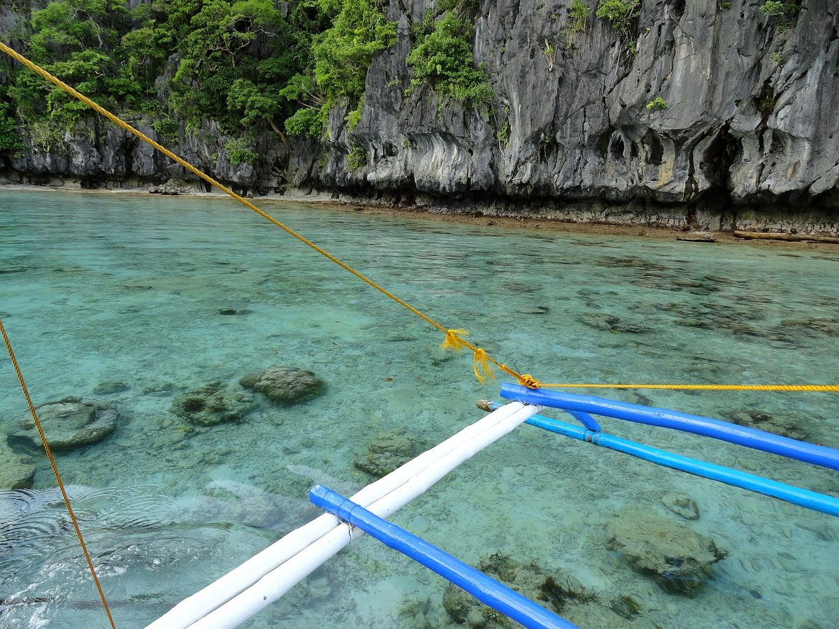Kayakers paddling into Big Lagoon on an el nido island hopping tour, turquoise water below limestone cliffs in Palawan, Philippines