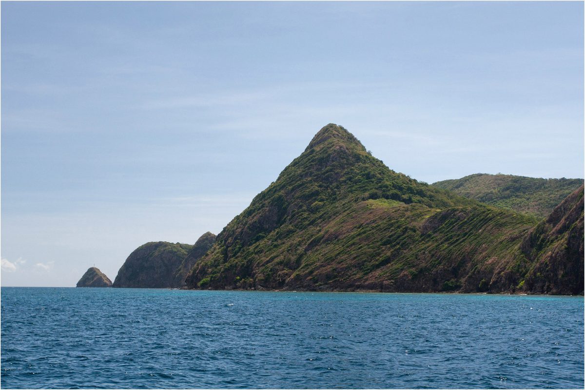 A green island rising from deep blue sea on the boat route between El Nido and Coron, Palawan, Philippines