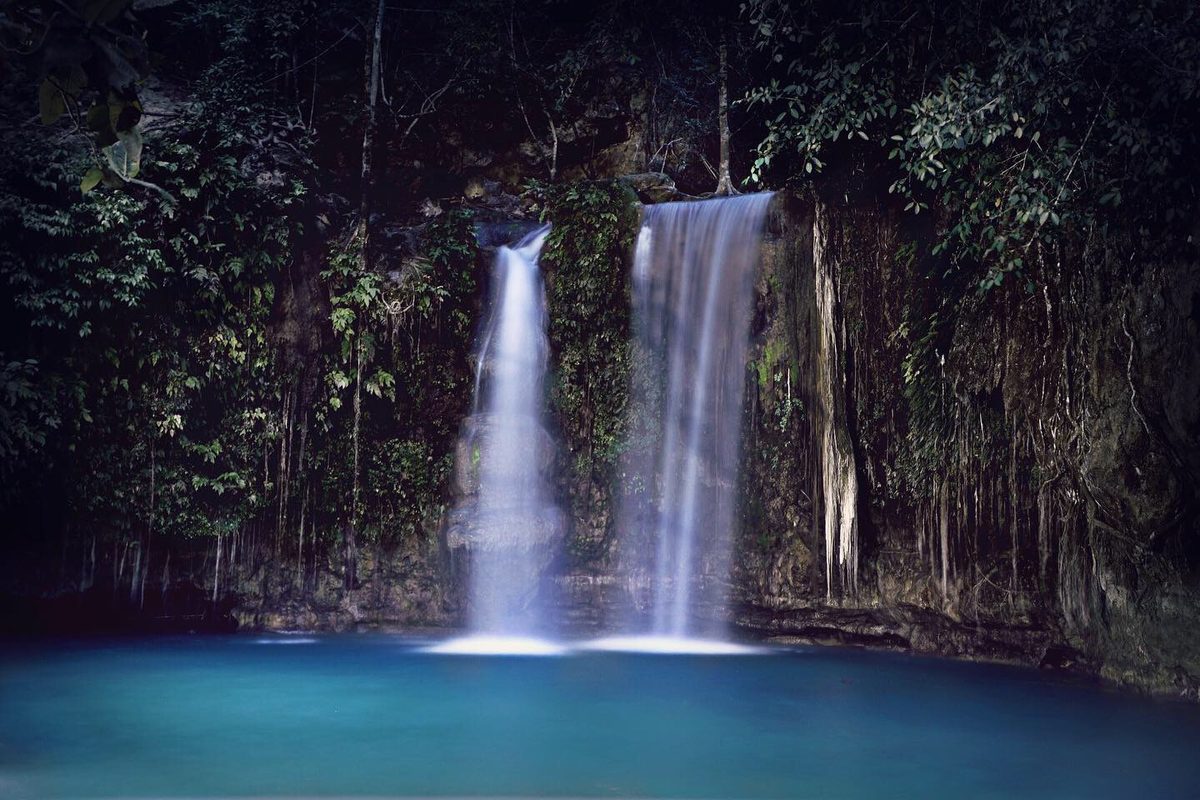 A cliff jumper leaping into a canyon pool on the Kawasan Falls canyoneering route