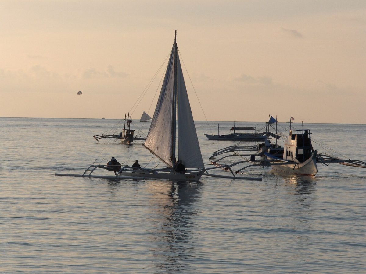 Traditional paraw sailboat with white sails gliding past Boracay at sunset