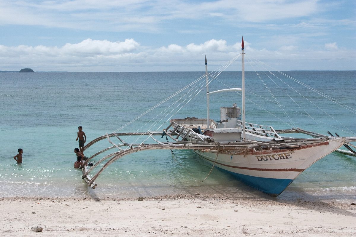 Traditional bangka outrigger boat moored off a Philippine beach used for island hopping