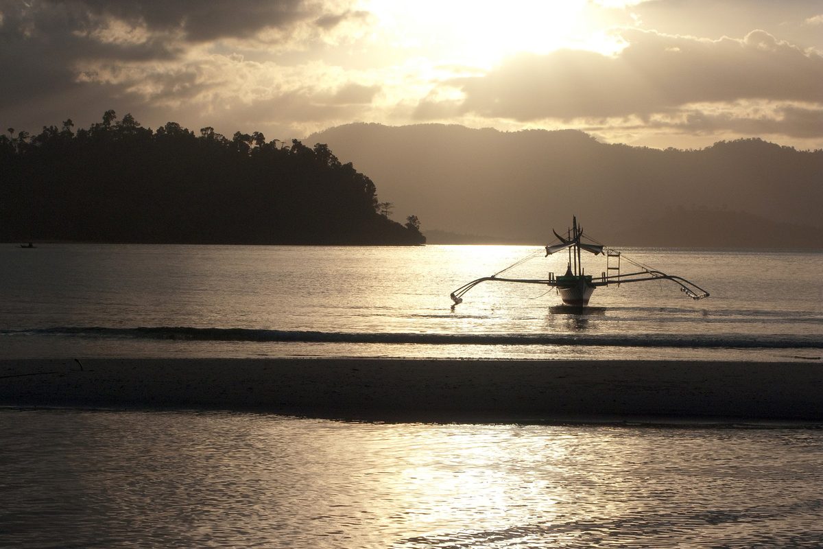 Quiet palm-lined beach and bangka outrigger boats at Port Barton, Palawan