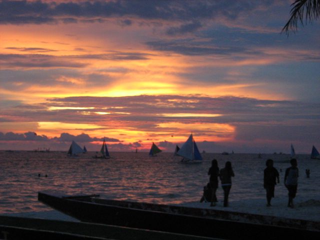 Sunset over a quiet Boracay beach beyond White Beach, with calm water and an outrigger boat