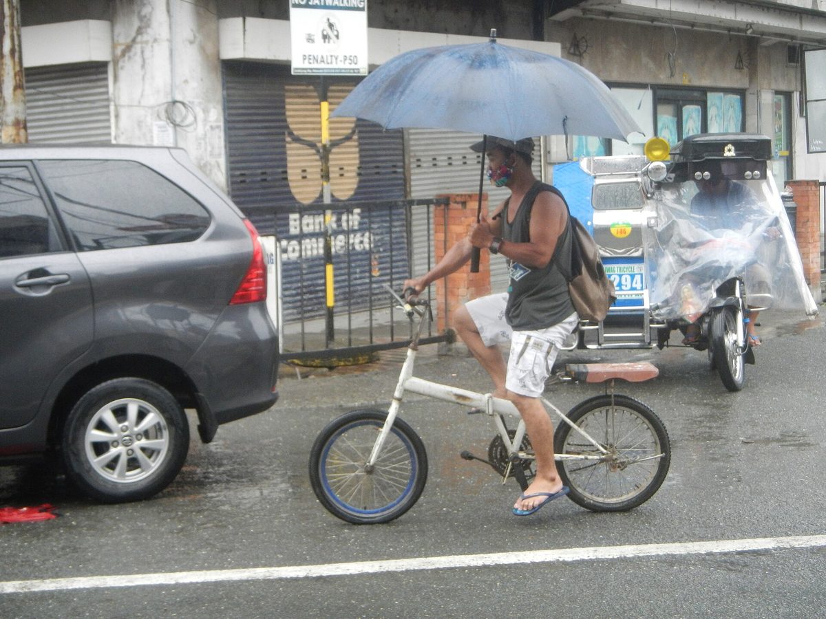 A man cycling under an umbrella through a wet street during a habagat downpour in the Philippines