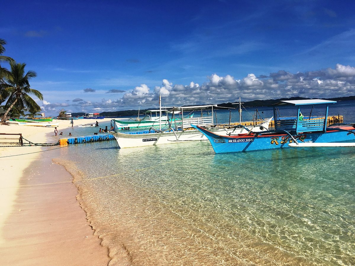 Outrigger boats on a white-sand, palm-fringed beach off Siargao, a classic island-hopping stop in the calm sunny season